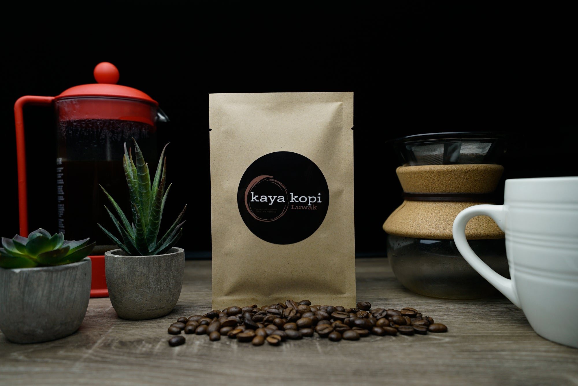 Kaya Kopi coffee bag with coffee beans and coffee-making equipment on a wooden surface.