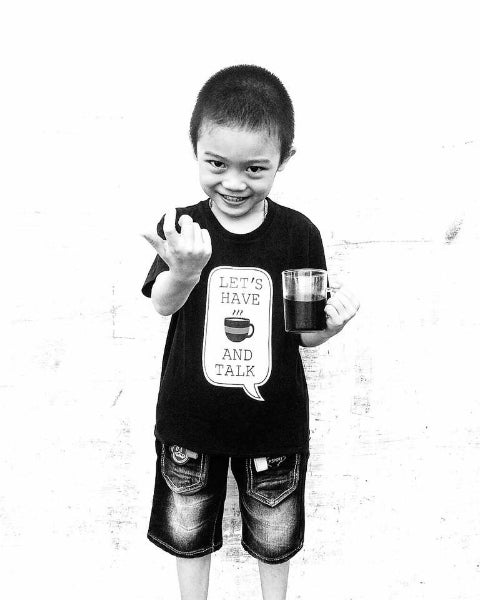 Child wearing a black t-shirt with text and holding a cup of luwak coffee