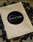 Kaya Kopi coffee package surrounded by coffee beans on a wooden surface