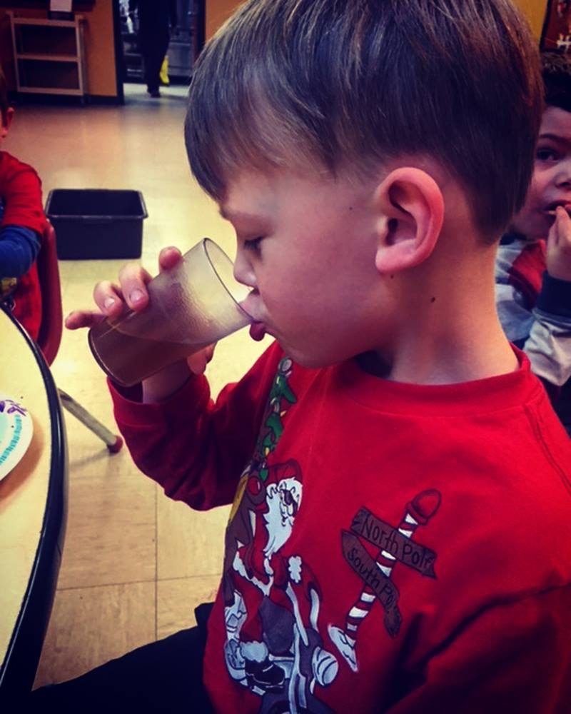 Child in a red shirt drinking coffee from a cup in an indoor setting