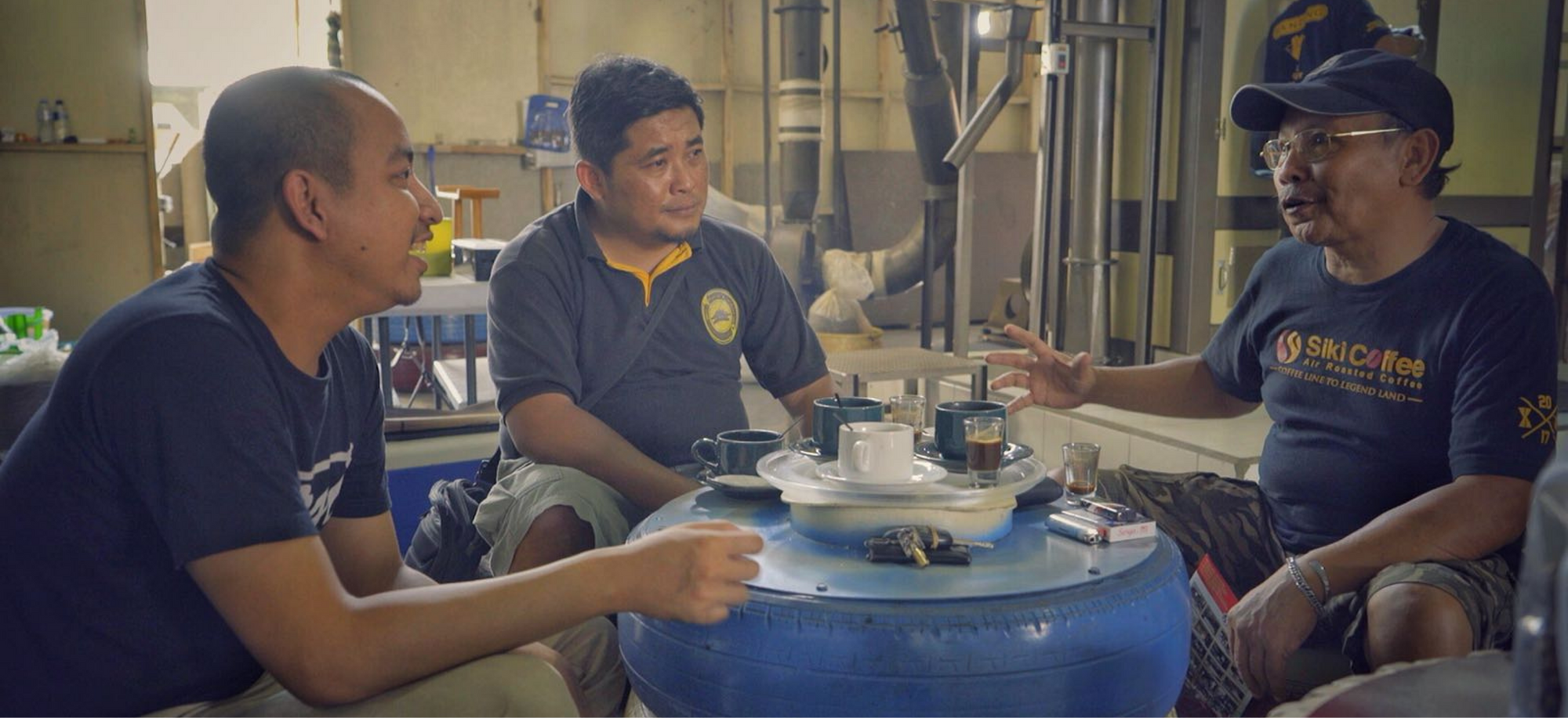 Three men enjoying Luwak coffee in a traditional coffee processing facility