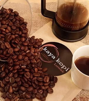 luwak Coffee beans, a coffee filter, and a cup of coffee with a 'kaya kopi' branded card on a textured surface.