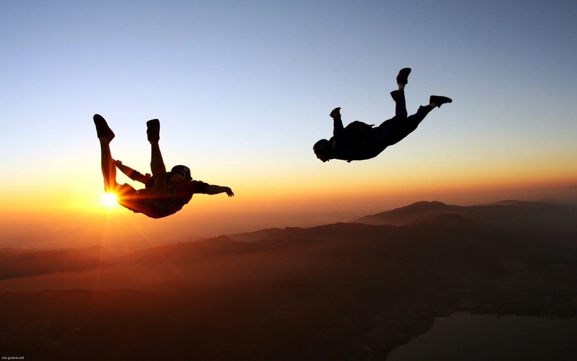 Two people skydiving against a sunset sky with mountains in the background